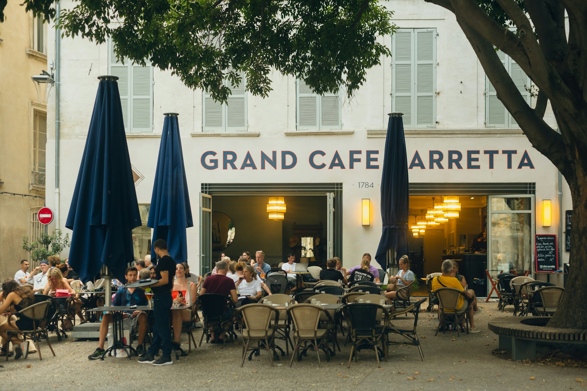 People sitting outside at the Grand Cafe Barretta in Avignon, France eating, talking, and drinking.